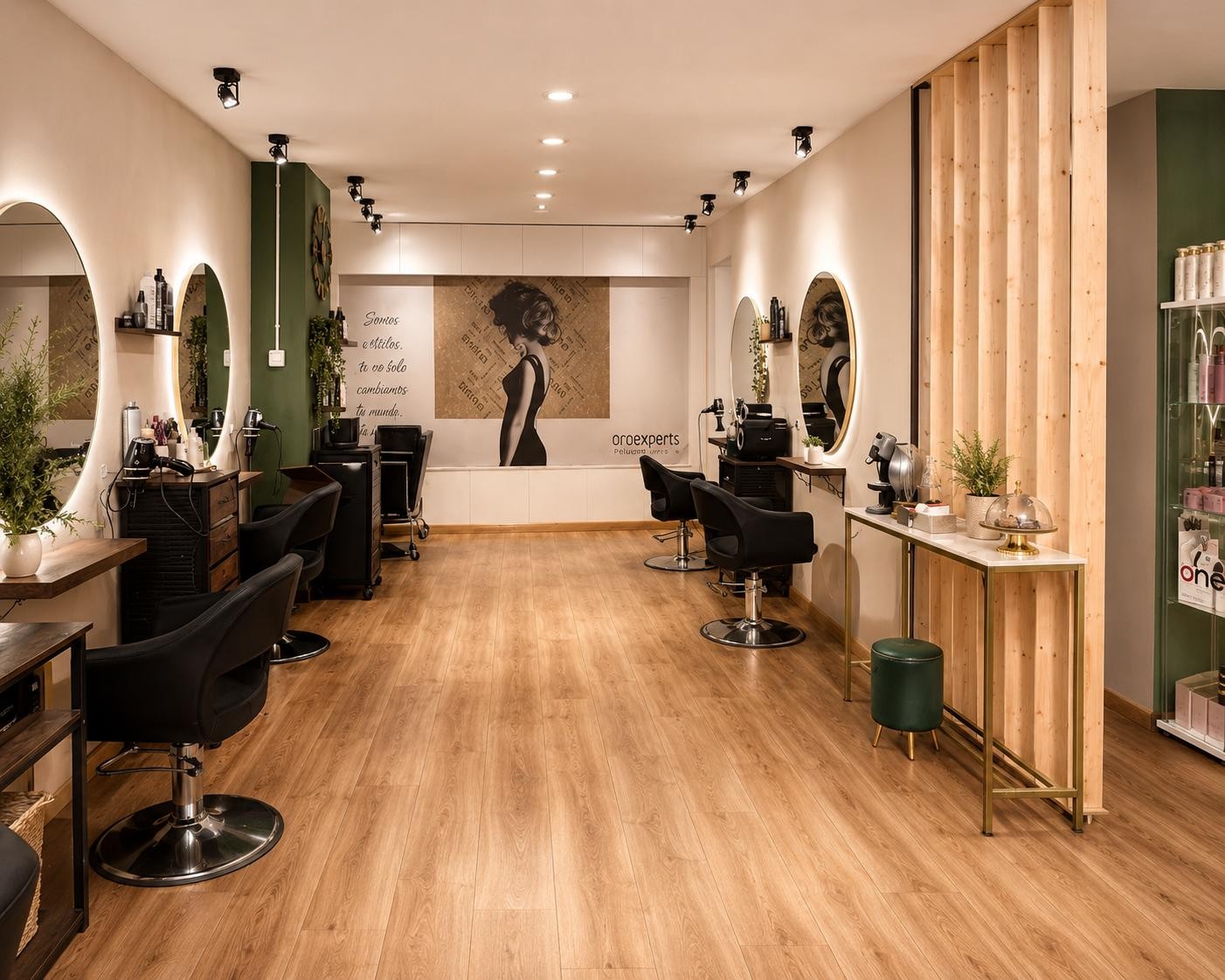 Interior del salón de peluquería, con los tocadores, la madera clara y la pared verde.